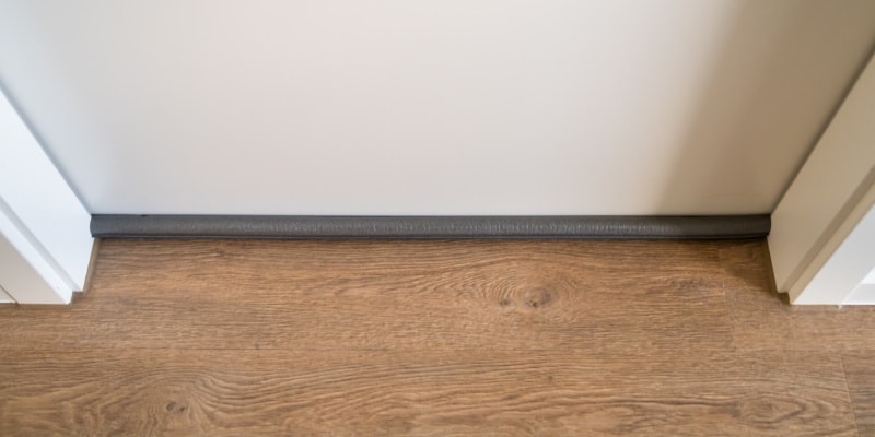 A white interior door with a fabric door sweep.