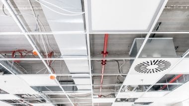 A suspended ceiling in the process of construction, with pipes and wires and lights.