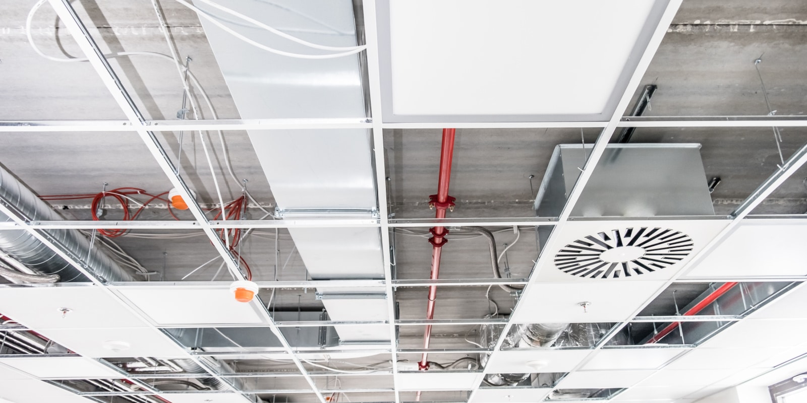 A suspended ceiling in the process of construction, with pipes and wires and lights.